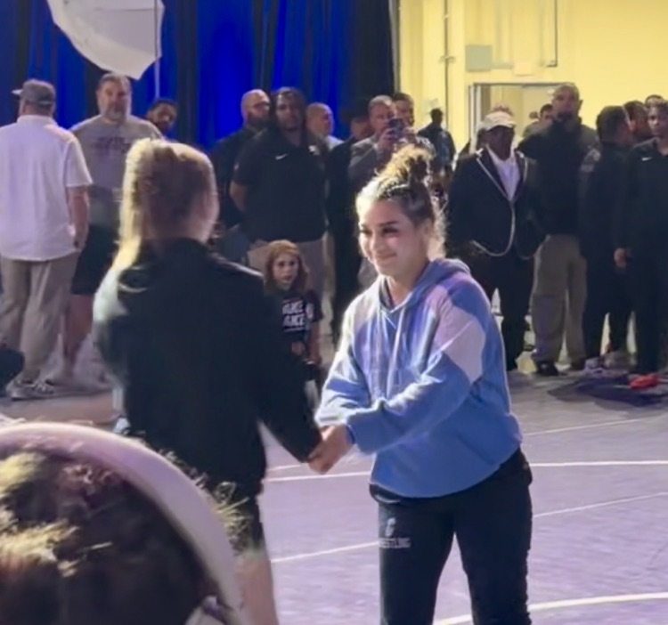 Wrestler in blue hoodie walks off the mat as scoreboard shows Genevieve Bellino winning 8–0 in the 5A 120 first place match.
