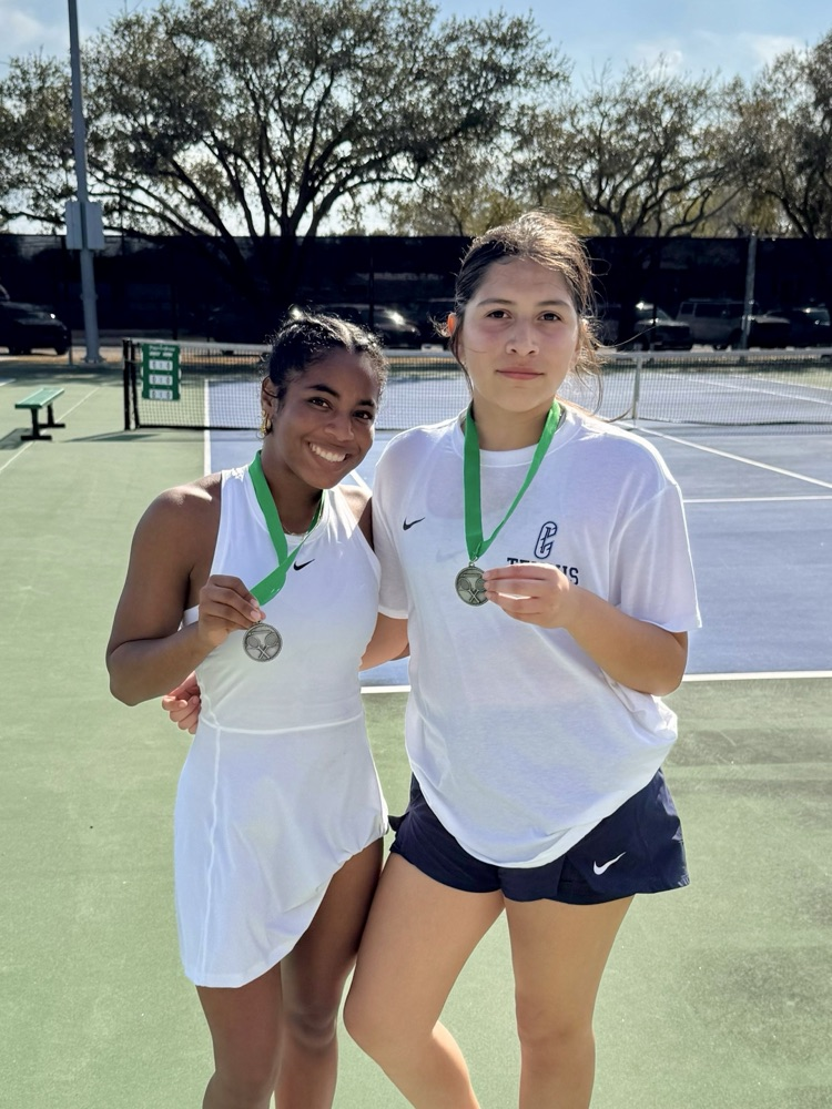 Tennis team posing on the court with medals after competing at the Bishop Tournament.