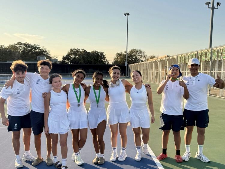 Tennis team posing on the court with medals after competing at the Bishop Tournament.