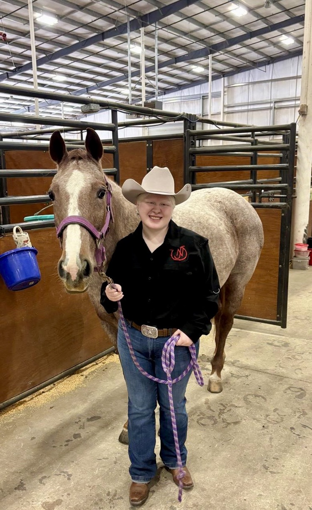 Student in western attire holding her horse in a barn aisle at a livestock show.