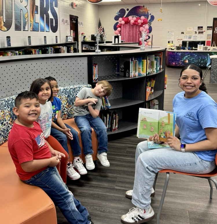 Alt text: High school students read picture books to elementary children in a colorful school library setting.