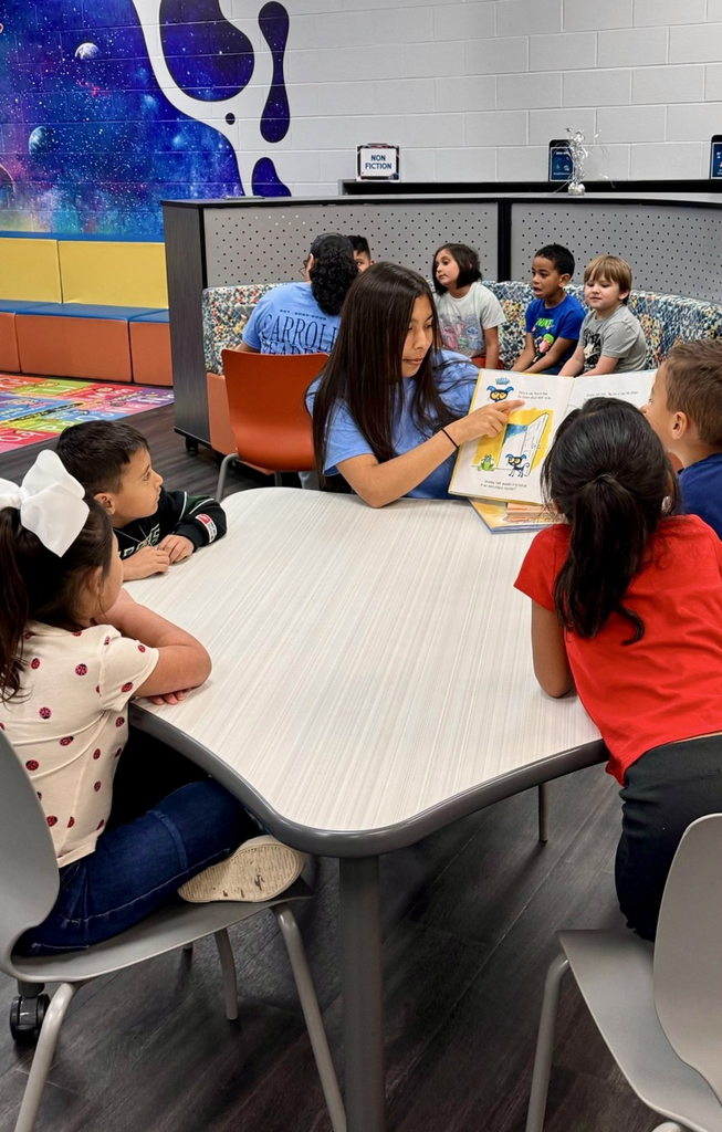 Alt text: High school students read picture books to elementary children in a colorful school library setting.