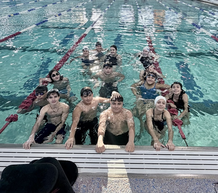 Middle and high school swimmers standing together in the pool during practice.