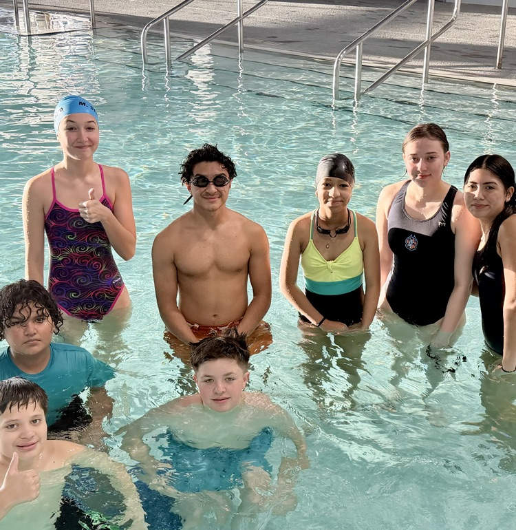 Middle and high school swimmers standing together in the pool during practice.