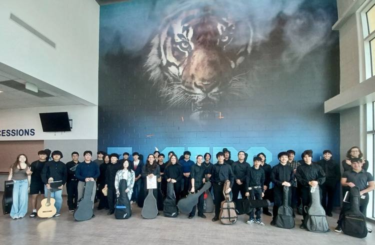 Students with guitar cases under tiger mural