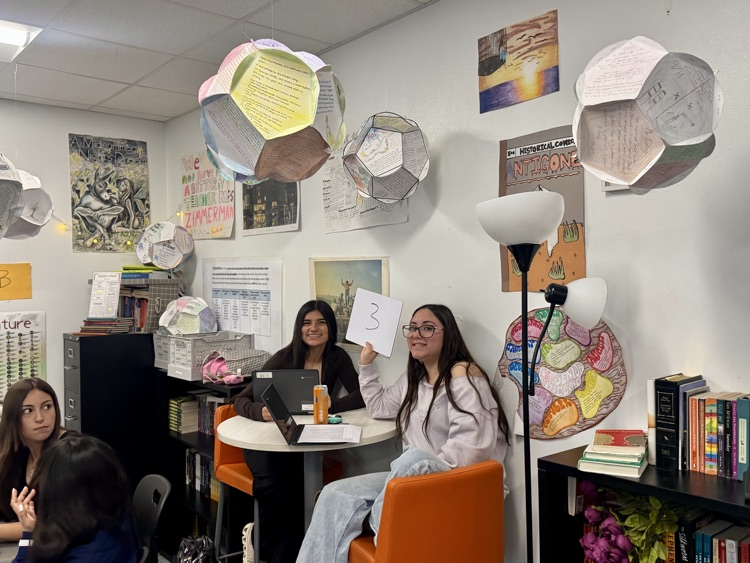 ⸻  Alt Text: Students in a classroom working on STAAR review activities, collaborating and studying together, with another group writing and reviewing work on colorful posters by a window.