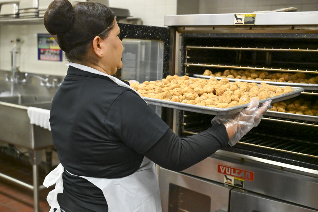 A person in uniform holding a tray of food in a kitchen. 