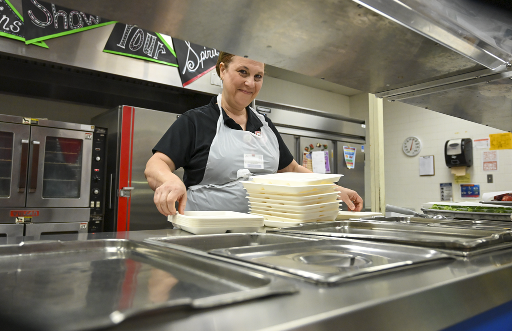 A woman in an apron stacks plates in a commercial kitchen.