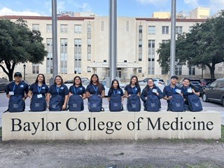 A group of people wearing blue shirts pose in front of a Baylor College of Medicine sign.