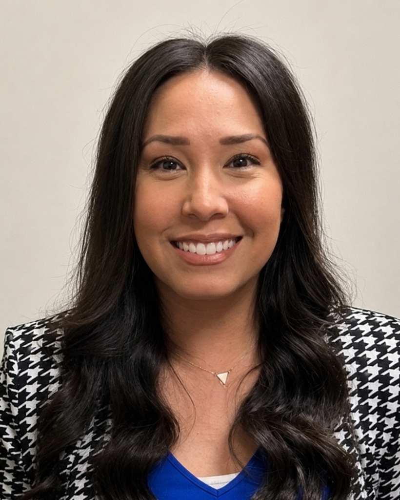 Woman with wavy dark hair, wearing a blue top, black and white checkered blazer, and a necklace.