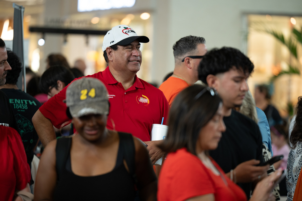 A crowd of people in a mall, some wearing red shirts, standing and conversing.