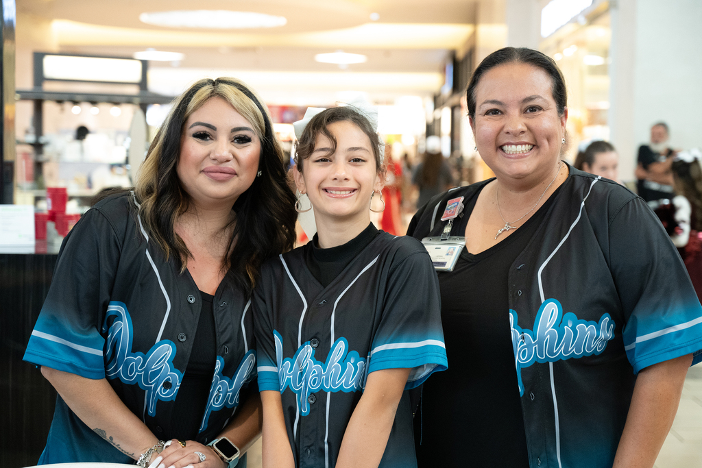Three women in baseball jerseys stand in a mall. One has a bracelet, another wears a necklace.