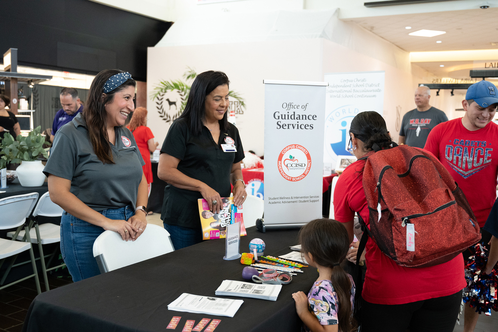 A group of people stands near a table with items on it, including a banner reading "Guidance Services".