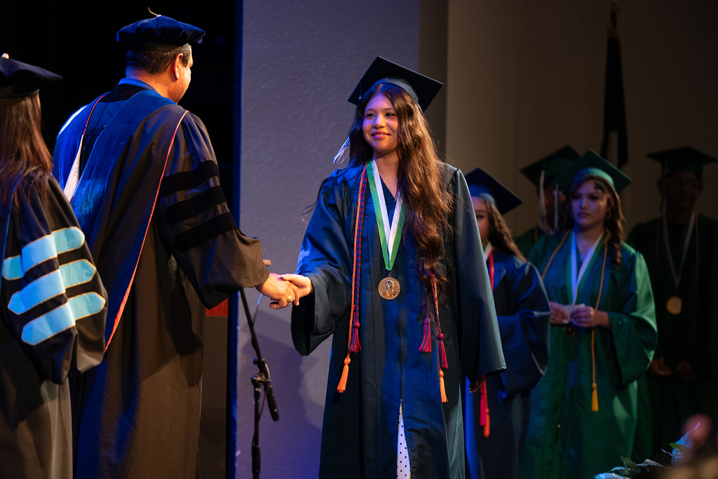 A person receiving a medal from a faculty member. They are both wearing caps and gowns.