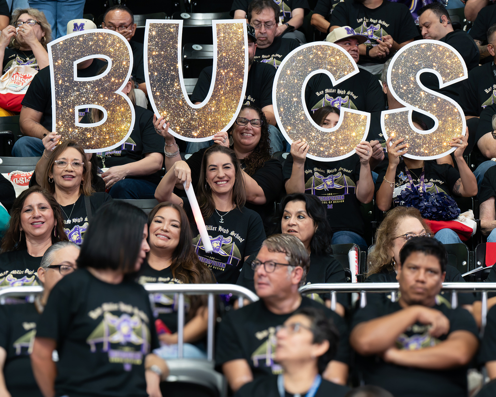 A crowd of people in black t-shirts, some holding up letters spelling "BUGS" in the air, with a cheering atmosphere.