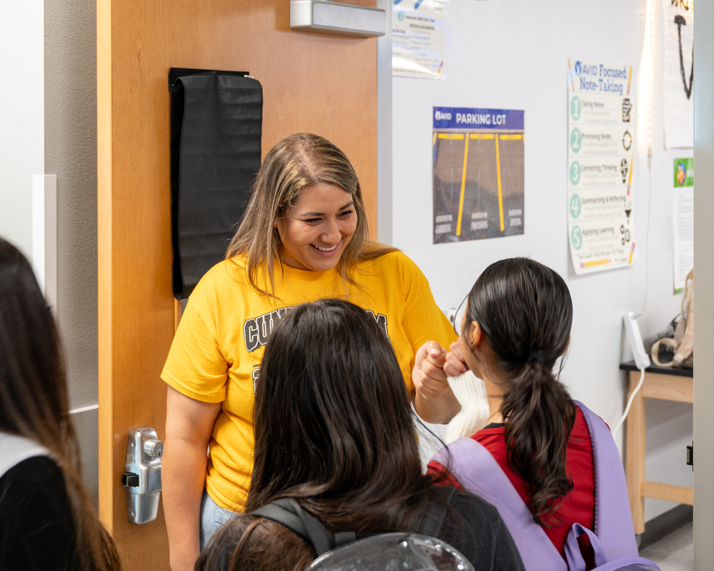 A woman in a yellow shirt stands in a room, smiling and talking to three women in front of her.