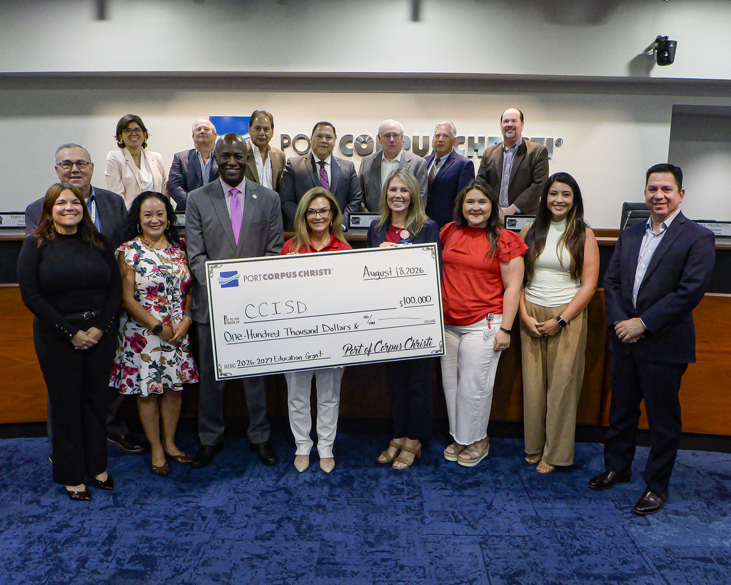 A group of adults standing and holding a large check in a conference room with a wooden desk.