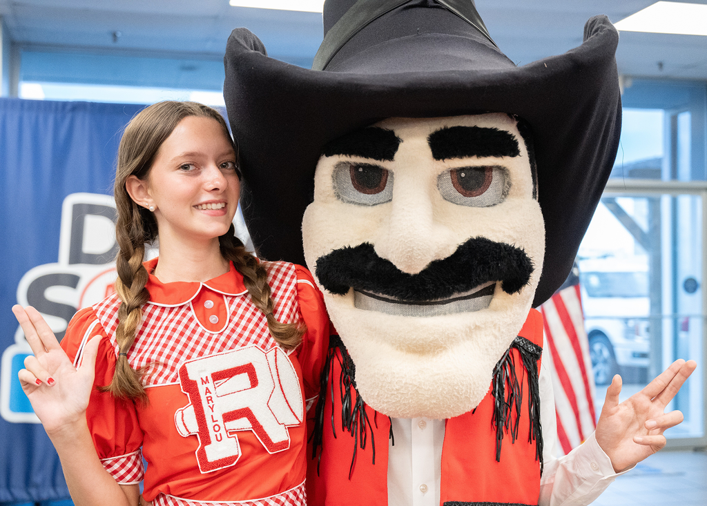 A young girl and a mascot with a black cowboy hat and a red shirt with white stripes.