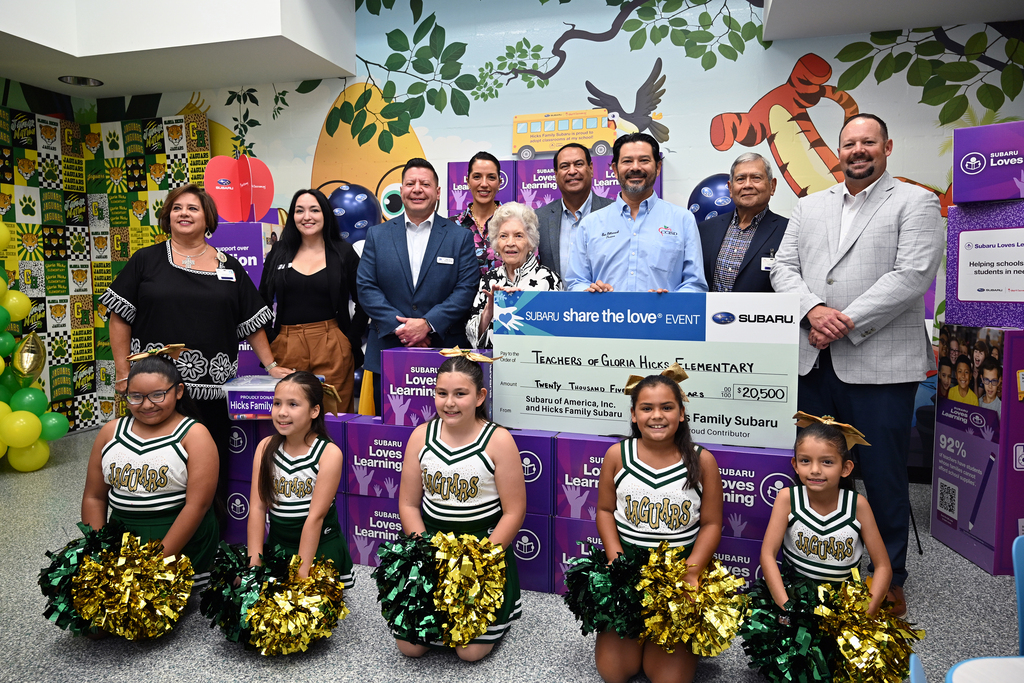 A group of adults and young cheerleaders pose for a photo. They hold a large check.