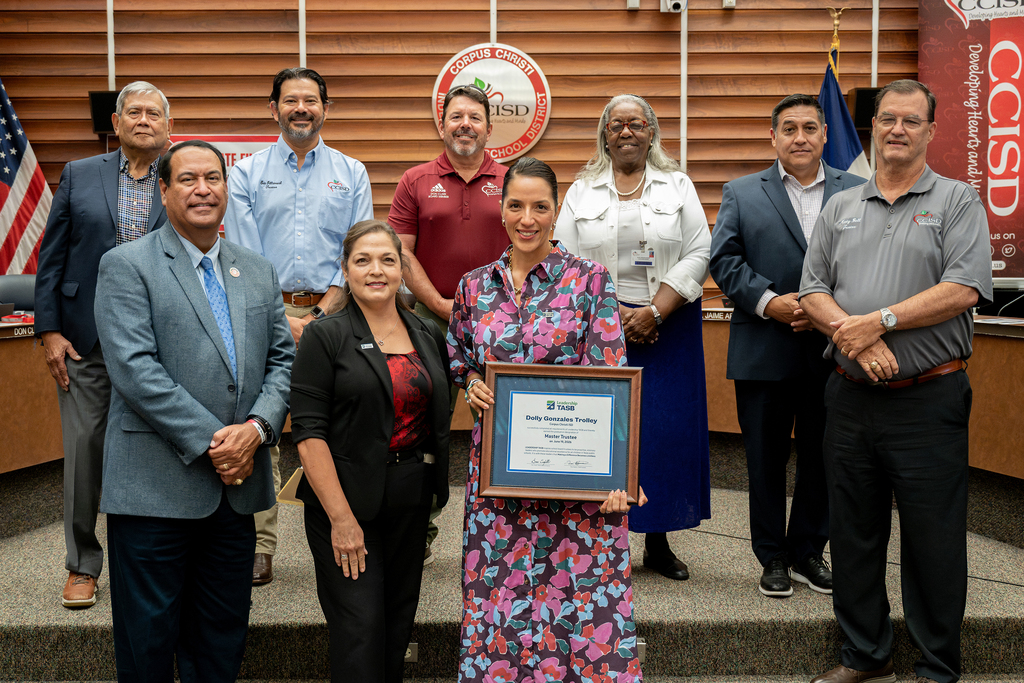 A group of people stand on a stage with a woman holding an award in front of them.