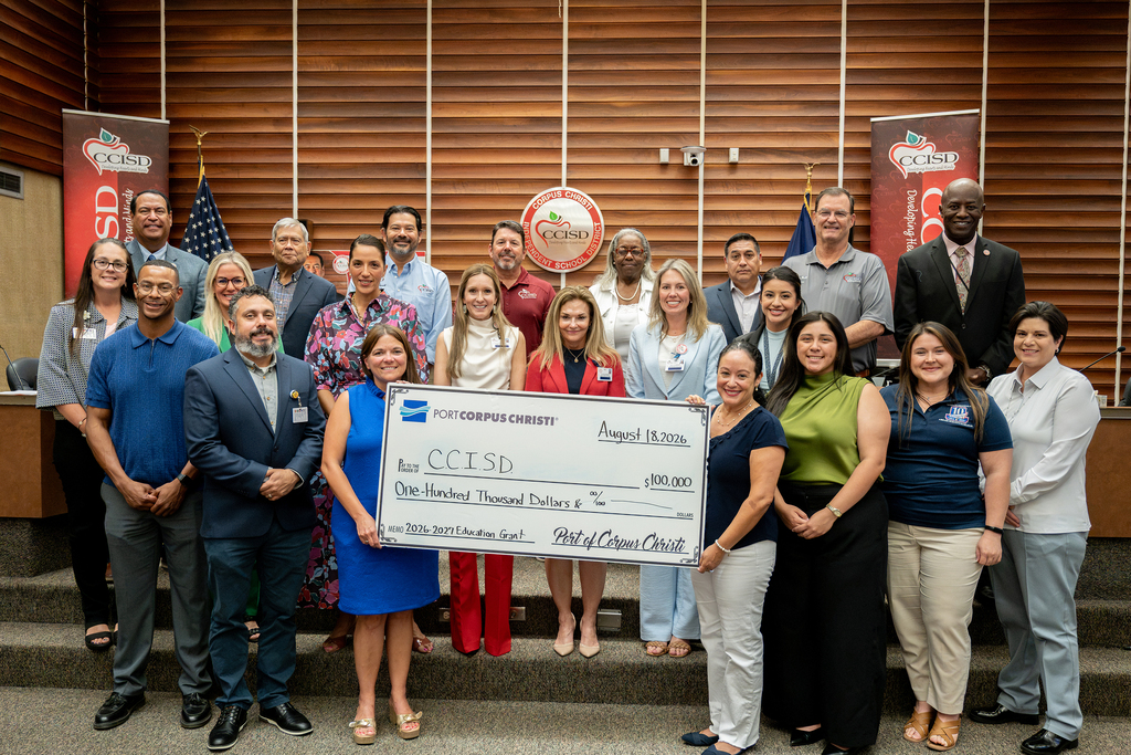A group of people stands in a room holding a large check. They are dressed in professional attire.