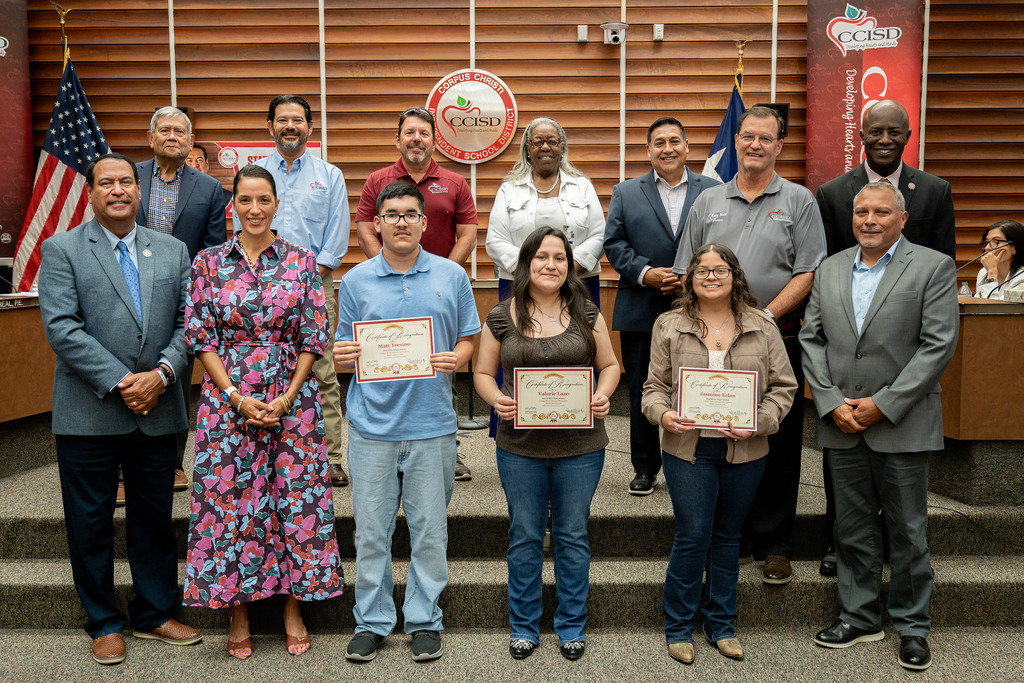 A group of people standing in front of a backdrop with flags. They are holding certificates.