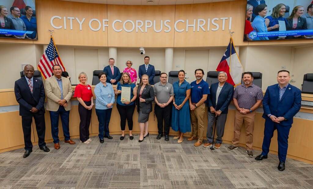 A group of people stands in a room with a "City of Corpus Christi" banner behind them.