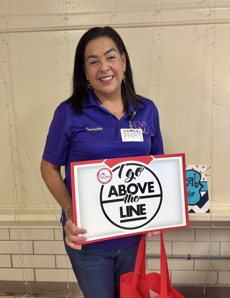Person in purple shirt holding a sign that says "1 go above the line" with a red handle bag.