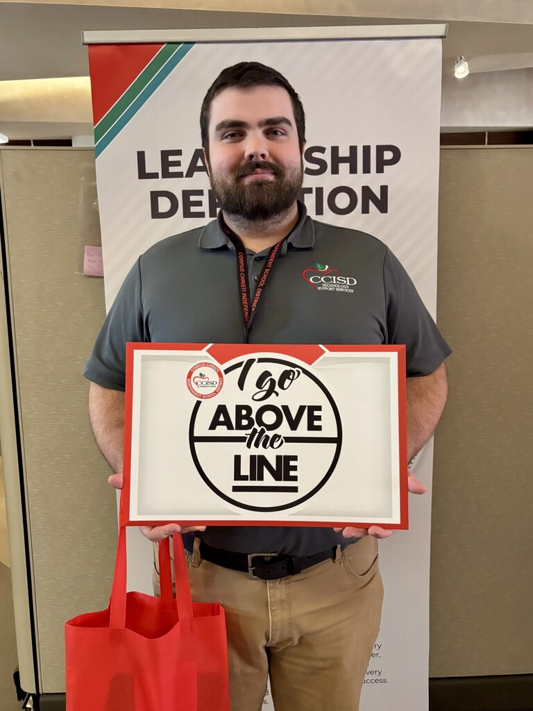 Man holds a sign with 120 Above the Line in front of a sign for Leadership Dedication.