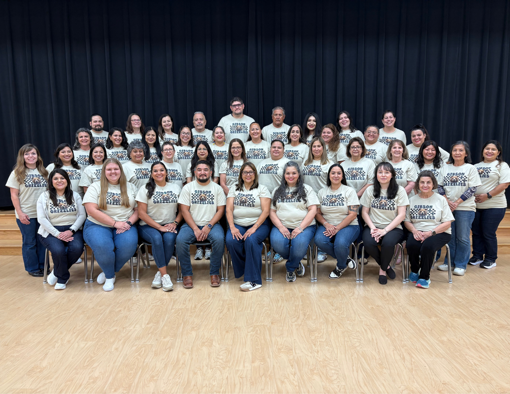 A group of people wearing light shirts and jeans gathered for a photo in front of a black curtain.
