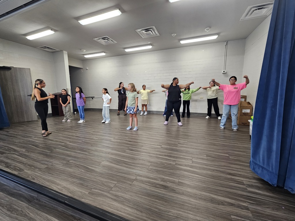 A group of individuals wearing casual clothing, engaging in exercise in a room with wooden floors.