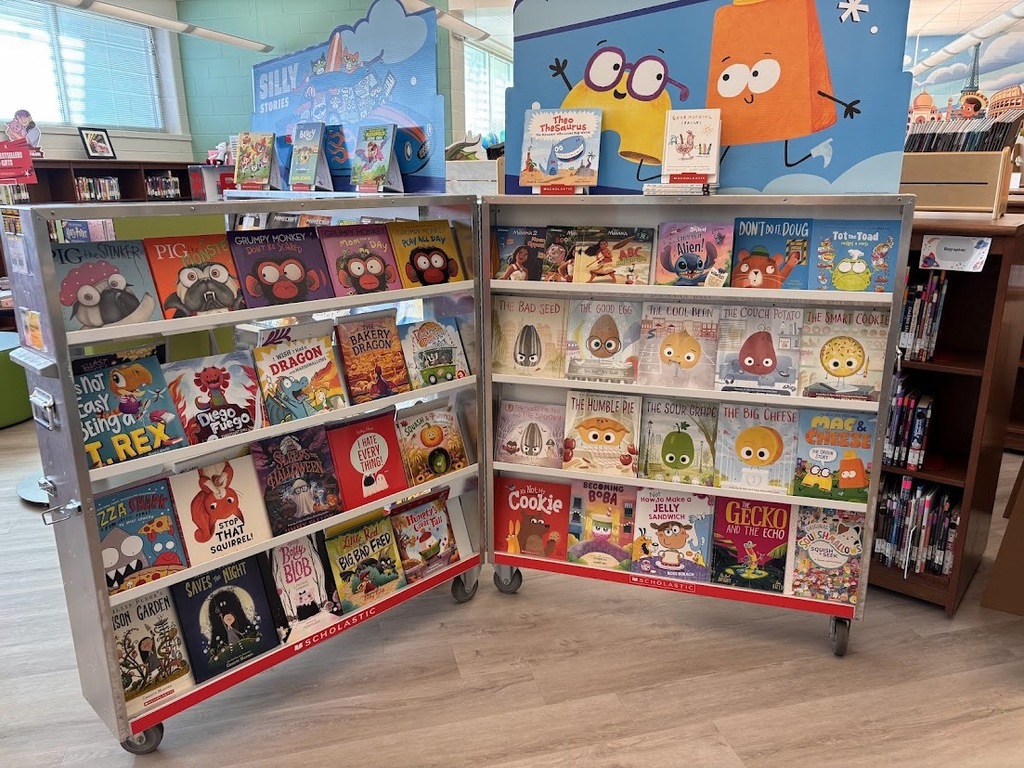 Two mobile book displays filled with colorful children's books in a brightly lit room with a wooden floor.