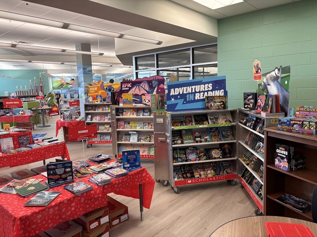 A library with several shelves filled with books. A table with books and other items on it.