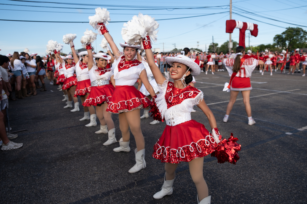 A group of cheerleaders, dressed in red and white uniforms, white boots, and white hats, perform.
