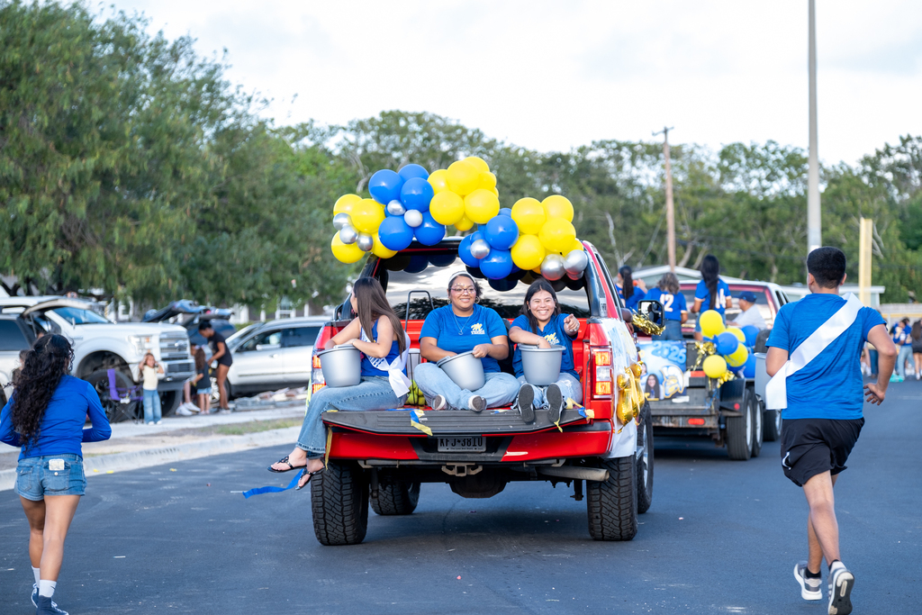 Group of people in blue and red shirts in a parade on a road with trees in the background.