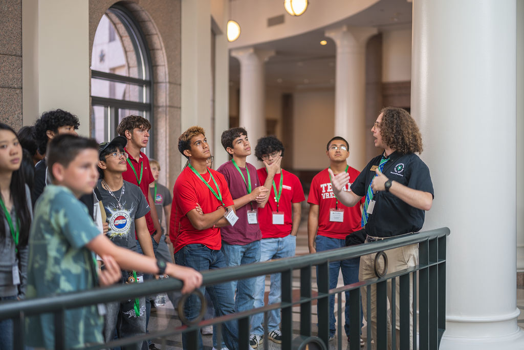 A group of students in red shirts stands in a hallway with a person in front of them.