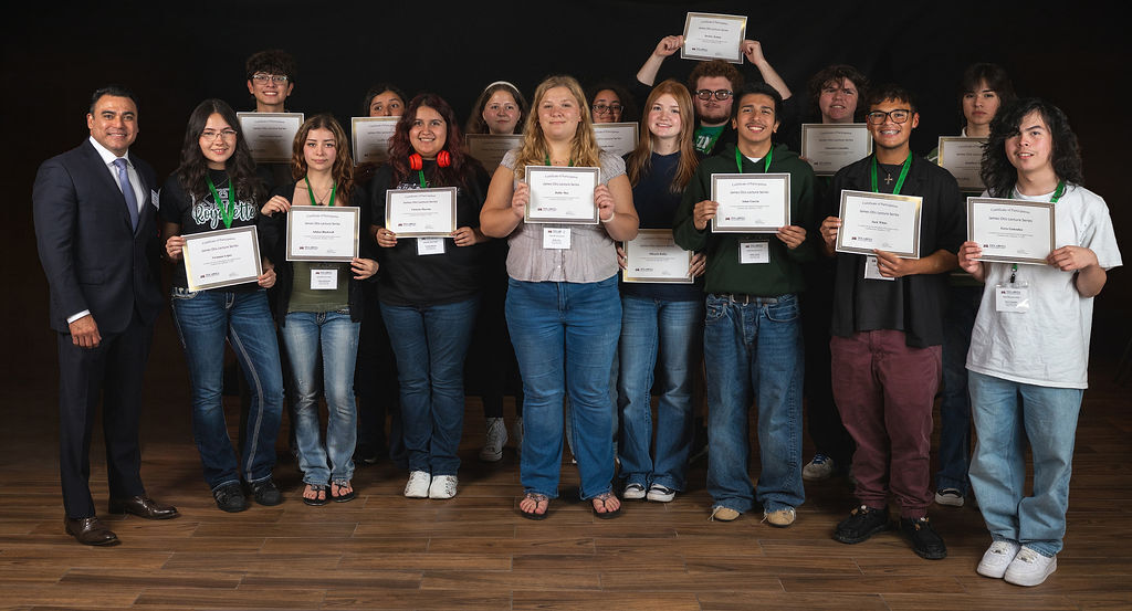 A group of students with certificates in hand pose for a photo with a man in formal attire.