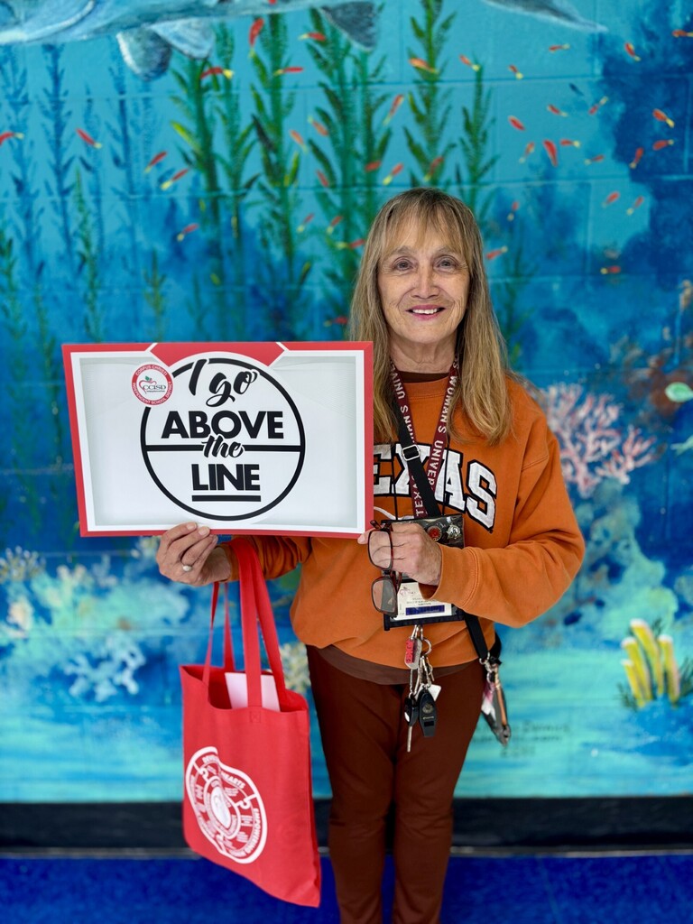 Woman holding a sign and red tote bag in front of a blue, aquatic-themed wall.