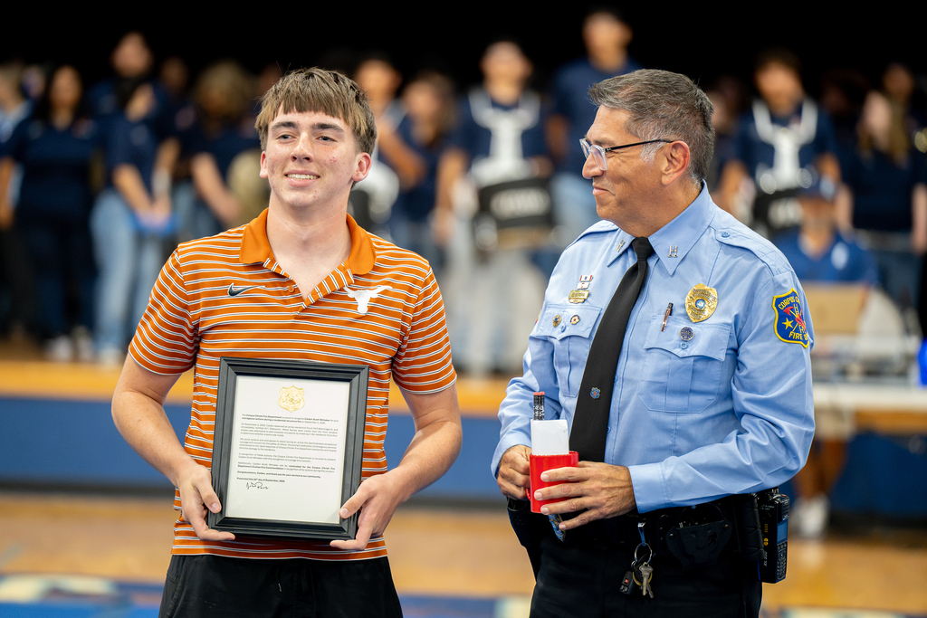 A man in an orange and white striped polo stands on a basketball court with others nearby.