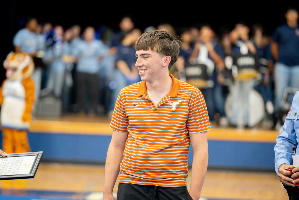 A man in an orange and white striped polo stands on a basketball court with others nearby.