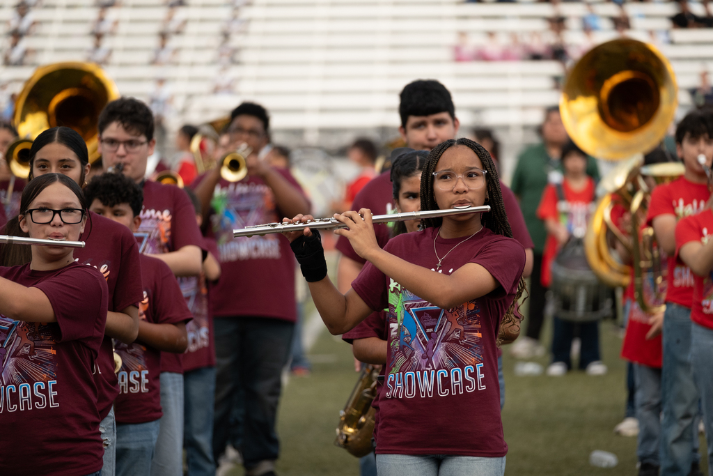 A school band practices on a field. A girl plays a flute, and others play trumpets and tubas.
