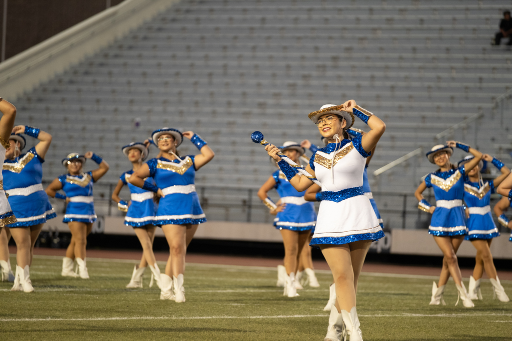 A group of cheerleaders performs on a football field with empty bleachers in the background.