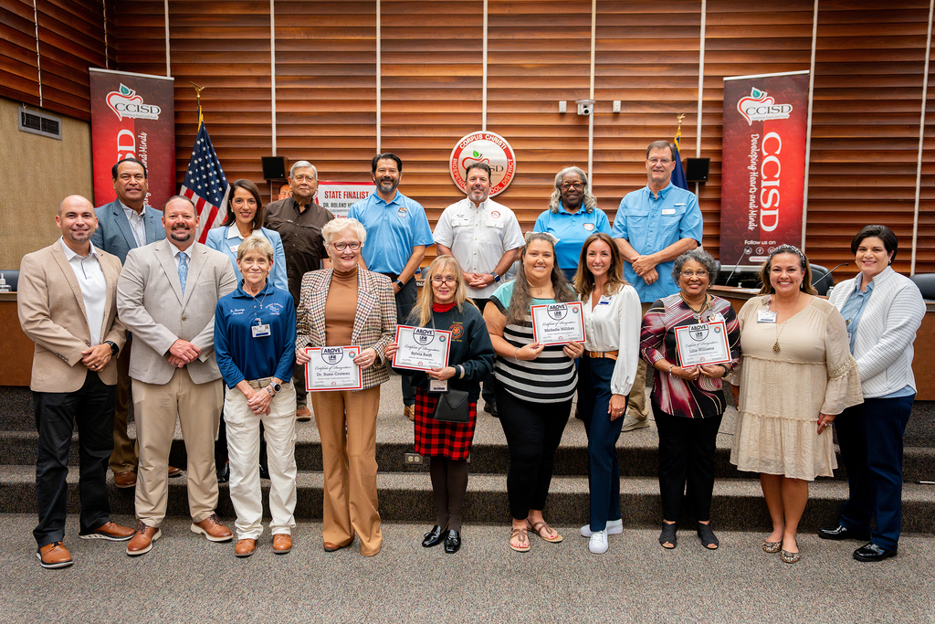 A group of people, some holding certificates, stands on a stage, posing for a photograph.