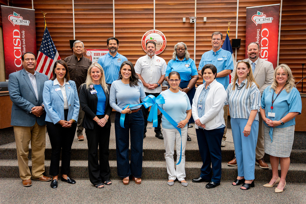 Group of people in blue shirts on steps, with two holding blue ribbon for a ribbon-cutting ceremony.