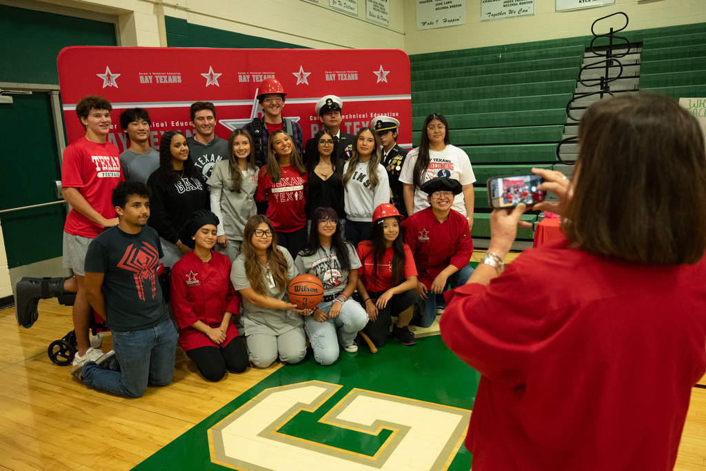 A group of students wearing red shirts pose for a photo on a basketball court with a red backdrop.