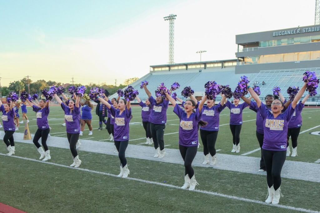 Group of cheerleaders in purple uniforms and white boots performing on a field at dusk.