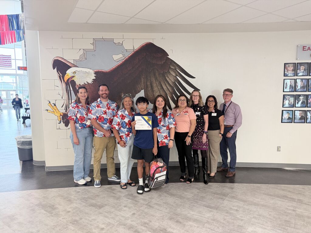 A group of people in matching shirts pose for a picture in a hallway. A large mural of an eagle is in the background.