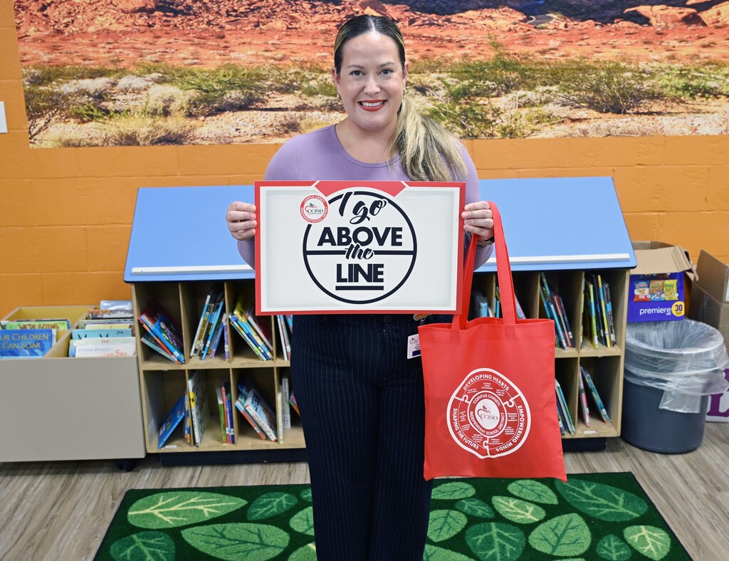 A woman holds a white sign with black text "Go Above the Line" in a room with shelves of books.