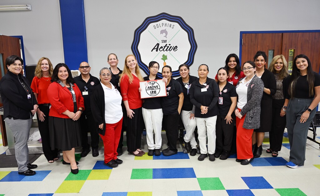 A group of women and men in matching red, white, and black uniforms stand in a room with a logo.