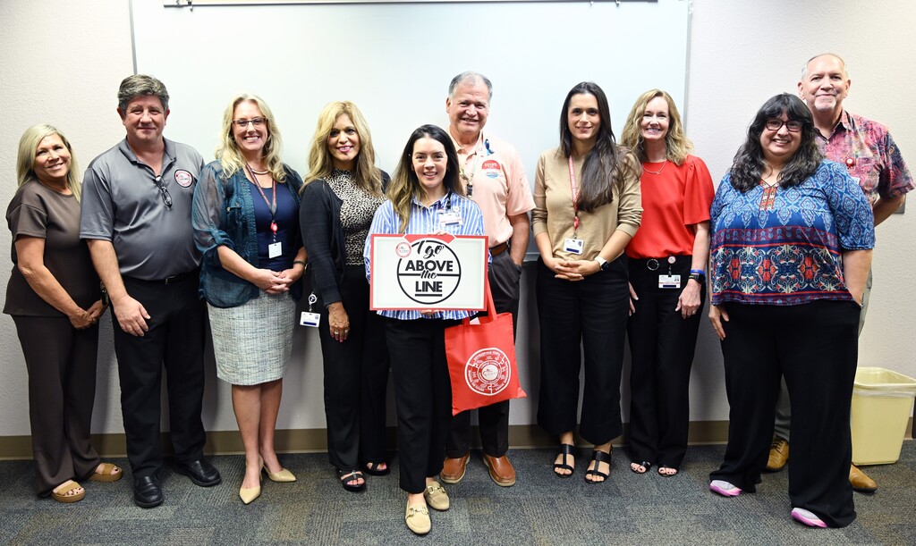 Group of people wearing casual clothing. One holds a sign. A woman stands in the middle, holding a red bag.